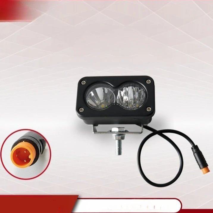 A black LED pod spotlight with two lenses and a wire is shown against a white background.