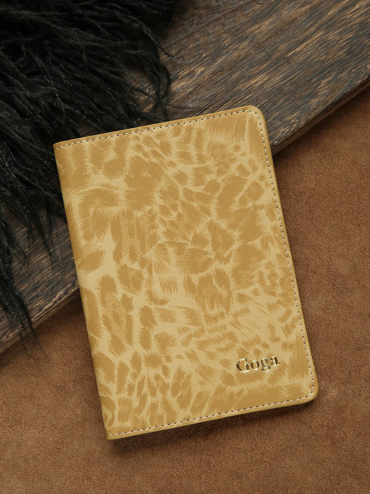 A tan leather passport holder with a leopard print pattern and the name Goga embossed on it, resting on a brown surface.
