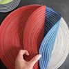 Gros plan d'un ensemble de dessous-de-verre et de sets de table ronds tissés dans des tons rouges, bleus et naturels.