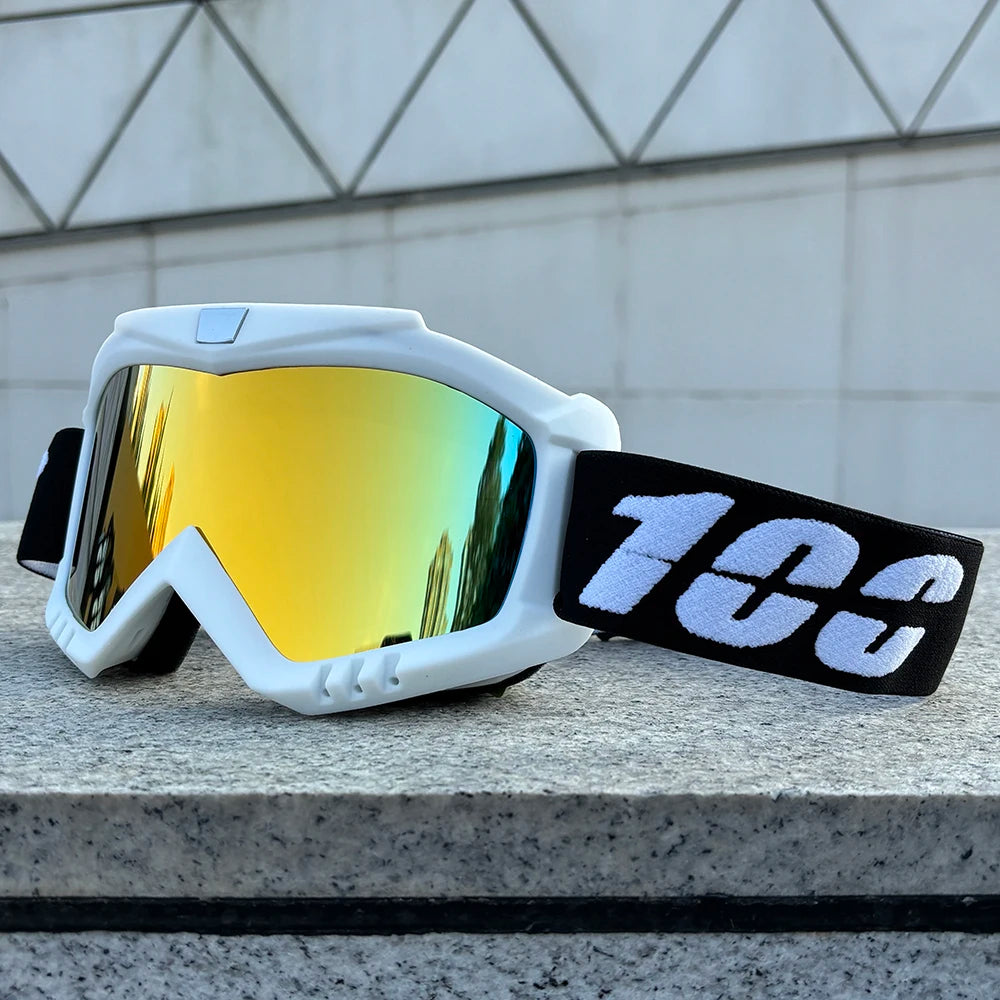 A pair of white windproof sports goggles with yellow-tinted lenses and a black strap resting on a gray stone surface.