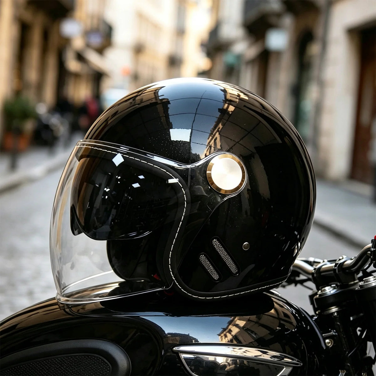 A glossy black two-lens retro motorcycle helmet resting on a dark motorcycle surface.