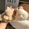 A close-up of a white plush bunny keychain with soft fur and a gold ring being held by a hand.