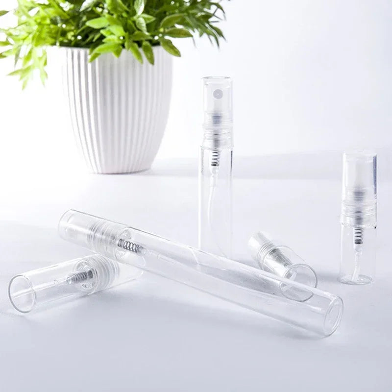 A set of clear glass perfume bottles and a refillable glass bottle are displayed next to a potted green plant.