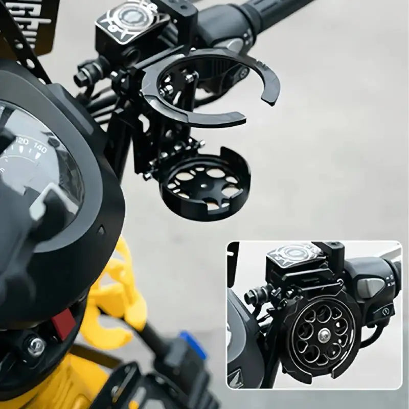 Close-up view of a black foldable motorcycle cup holder bracket mounted on a yellow handlebar.
