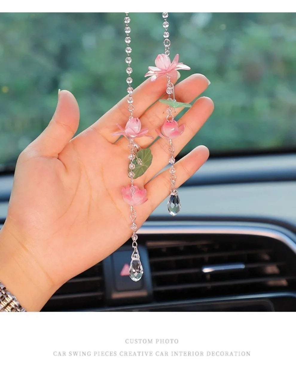 A hand holds a pink lotus car pendant ornament featuring delicate pink flowers and clear beads.