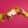 Une main tenant un support de téléphone en silicone jaune contre un fond rose.