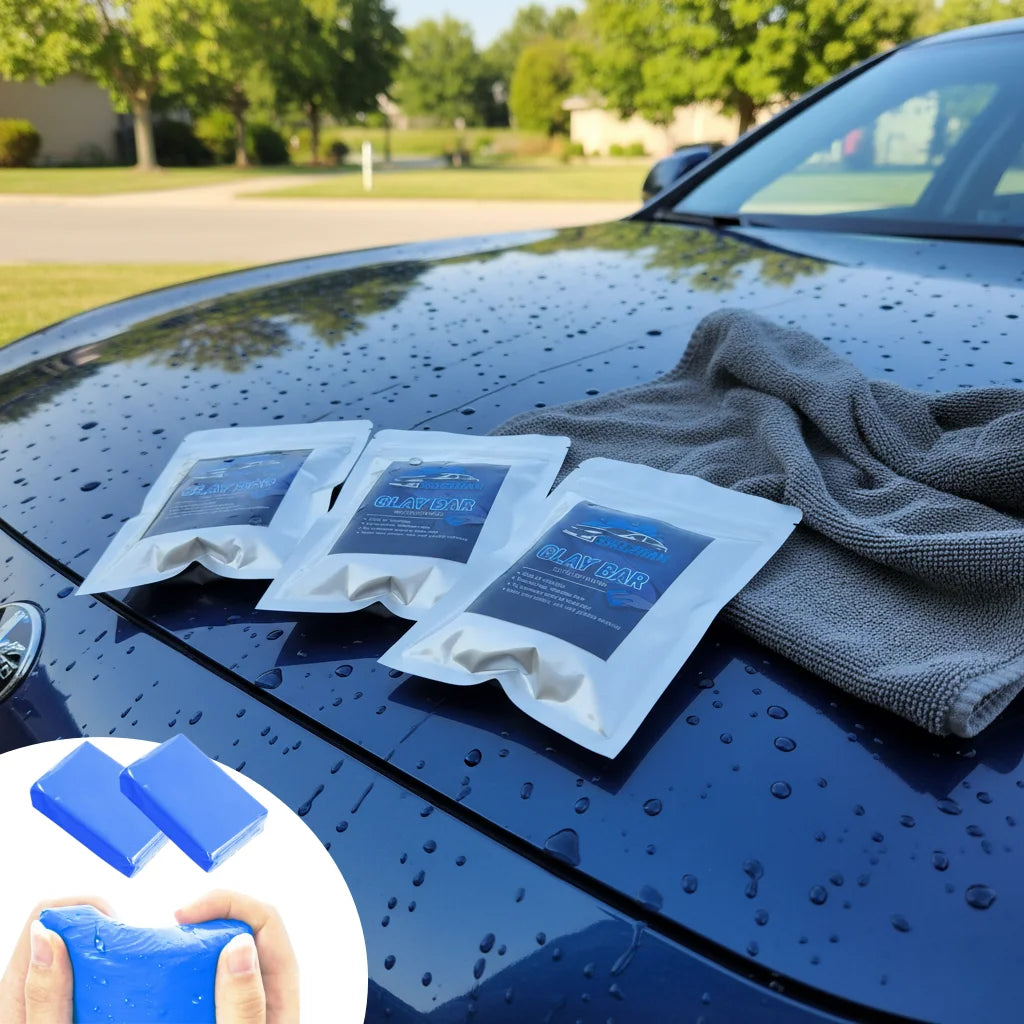 Several packs of clay bar are placed on a wet black car hood next to a gray towel and a hand holding a blue detailing tool.