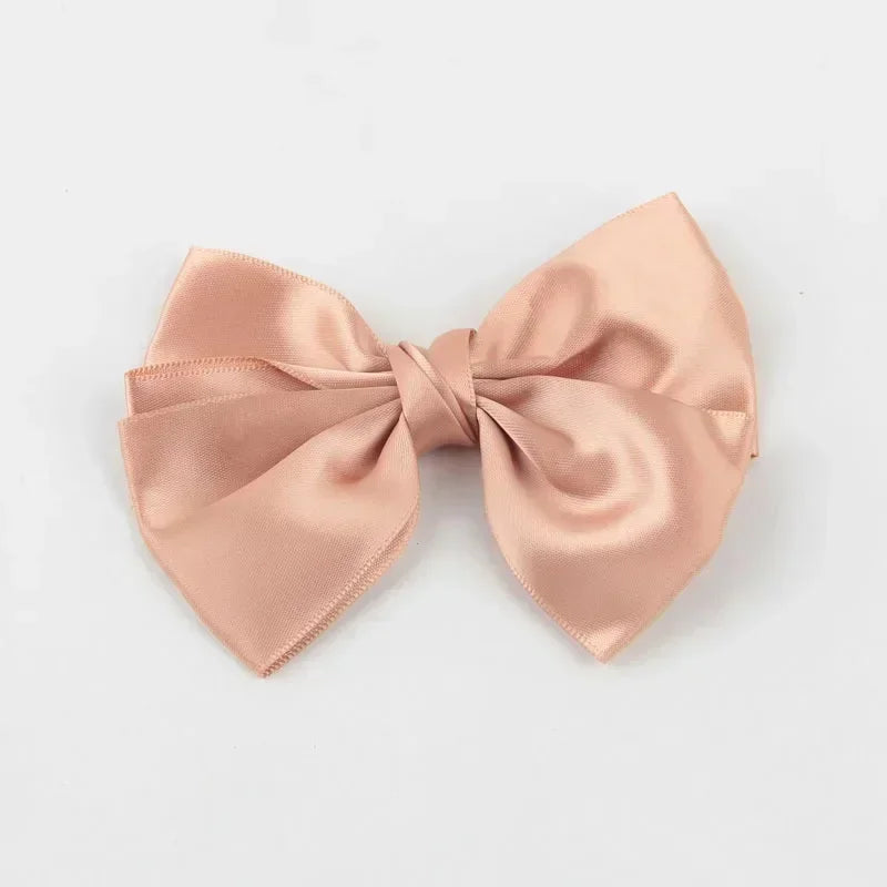 A soft blush pink silk hair bow tied in a classic bow shape.