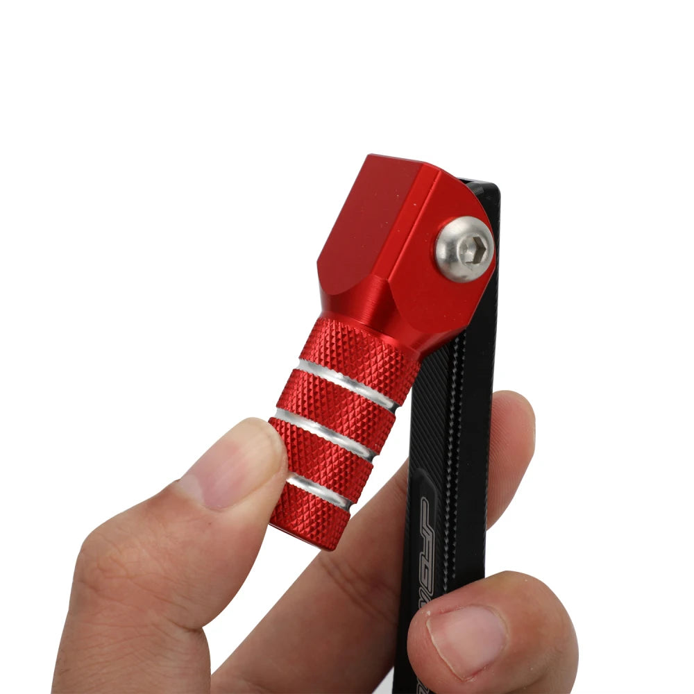 A hand holds a red and black CNC foldable aluminum gear shift lever for motorcycles.