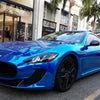 A bright blue muscle car parked on a street with storefronts in the background.