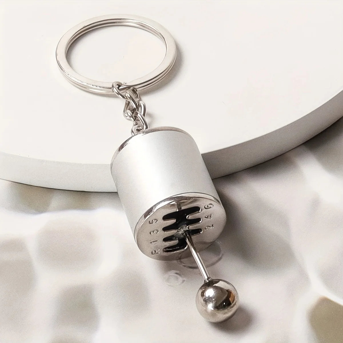 Silver keychain featuring a cylindrical metal component with an engraved symbol and a spherical charm.