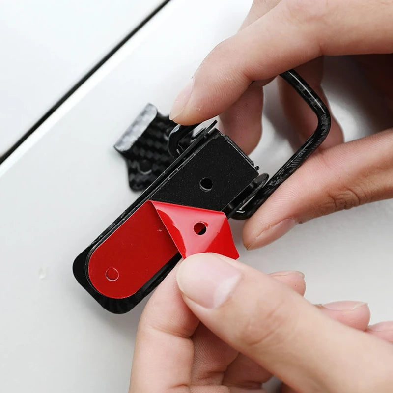 A hand is holding a black car trunk pull buckle repair clip with a red component against a white background.