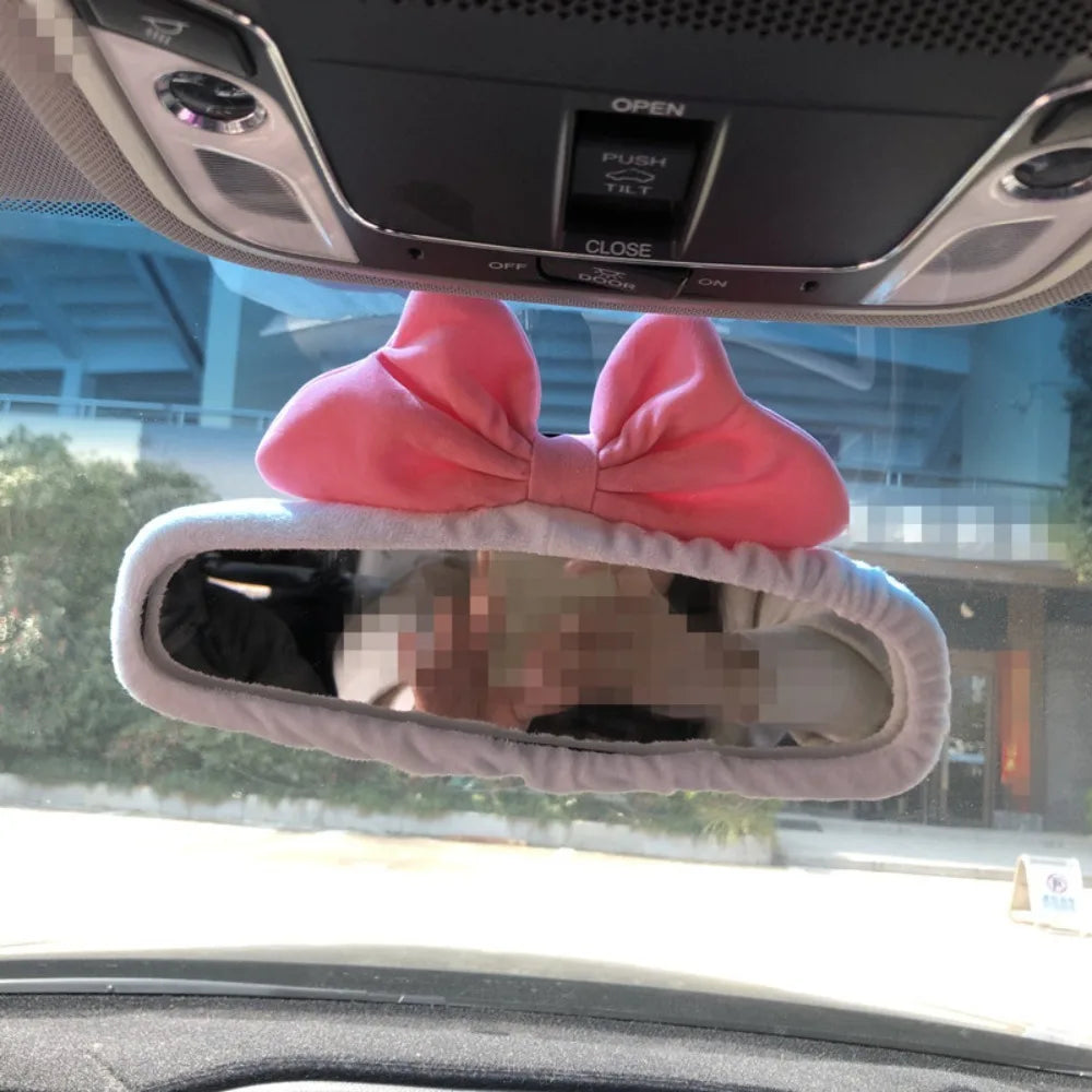 A pink bow shaped cover is placed over a rearview mirror inside a car.