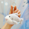 A hand holds a white plush bunny keychain with soft fur and a gold ring against a light blue background.