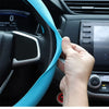 A hand is adjusting a bright blue silicone steering wheel cover on a black car steering wheel.