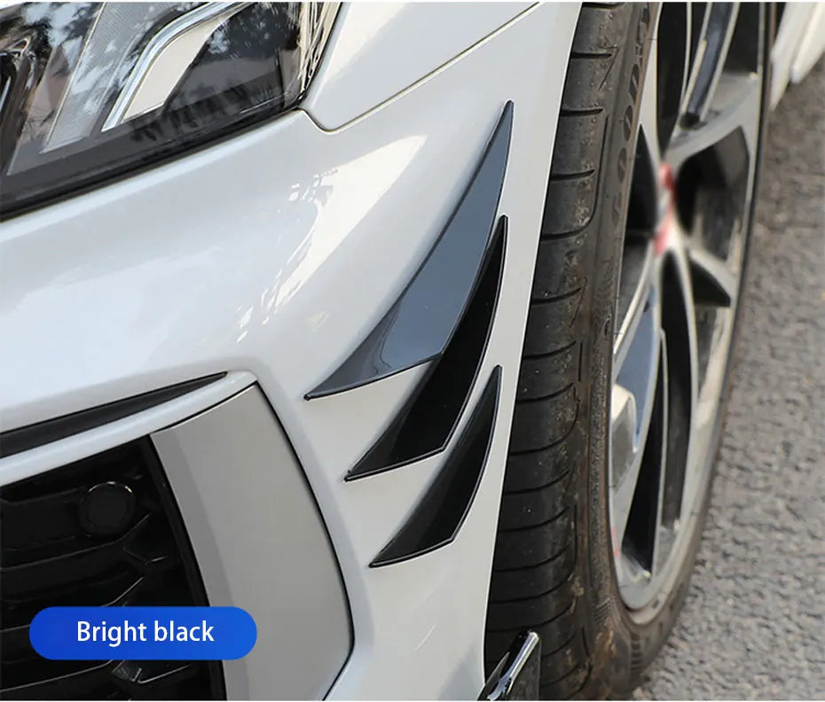 Close-up of a white car's front fender and wheel showing bright black spoiler fins.