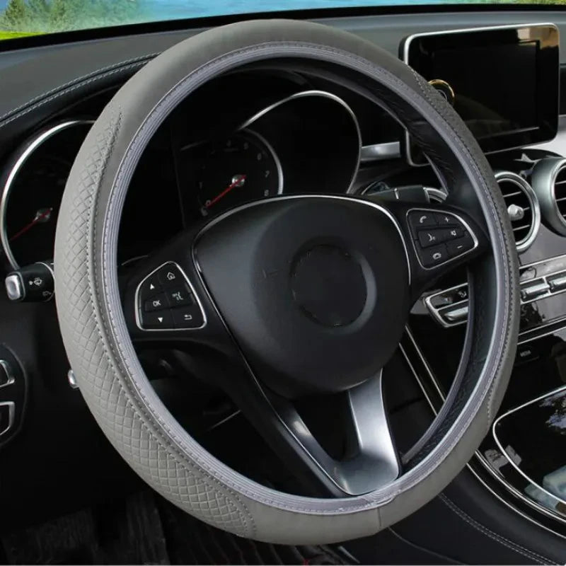 Close-up view of a black steering wheel with a light gray anti-slip leather cover inside a car interior.