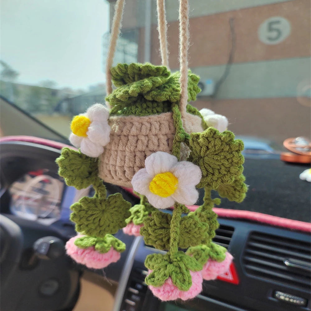 A strawberry crochet hanging decor made of green and white yarn is displayed on a car dashboard.