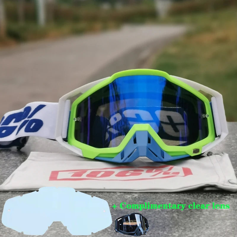 A pair of bright lime green and blue motocross goggles resting on a gray surface with an extra clear lens included.