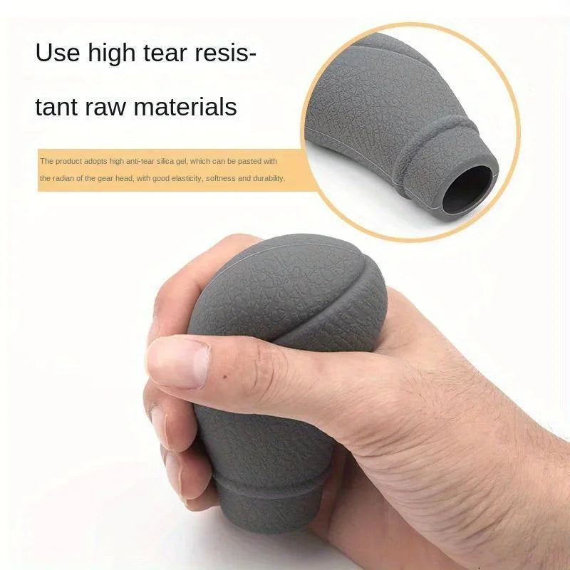 A hand is holding a gray, textured car gear shift knob and handbrake cover set.