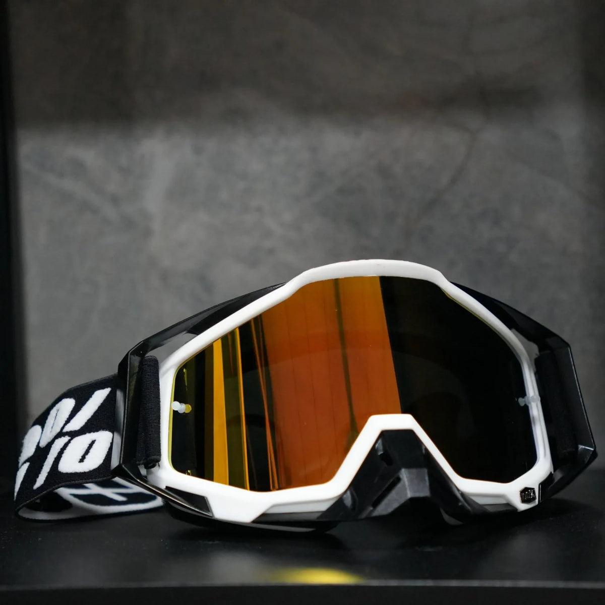 A pair of black and white high-performance motocross goggles with orange tinted lenses resting on a dark surface.