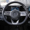 Close-up view of a black steering wheel with carbon fiber grips and controls inside a car
