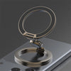 A close-up of a bronze magnetic phone ring stand with a dual-sided grip resting on a smartphone.