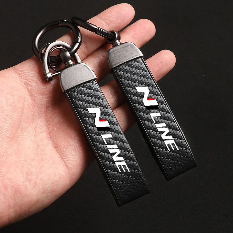 A pair of black carbon fiber style keychains with silver metal clasps are held in a hand.