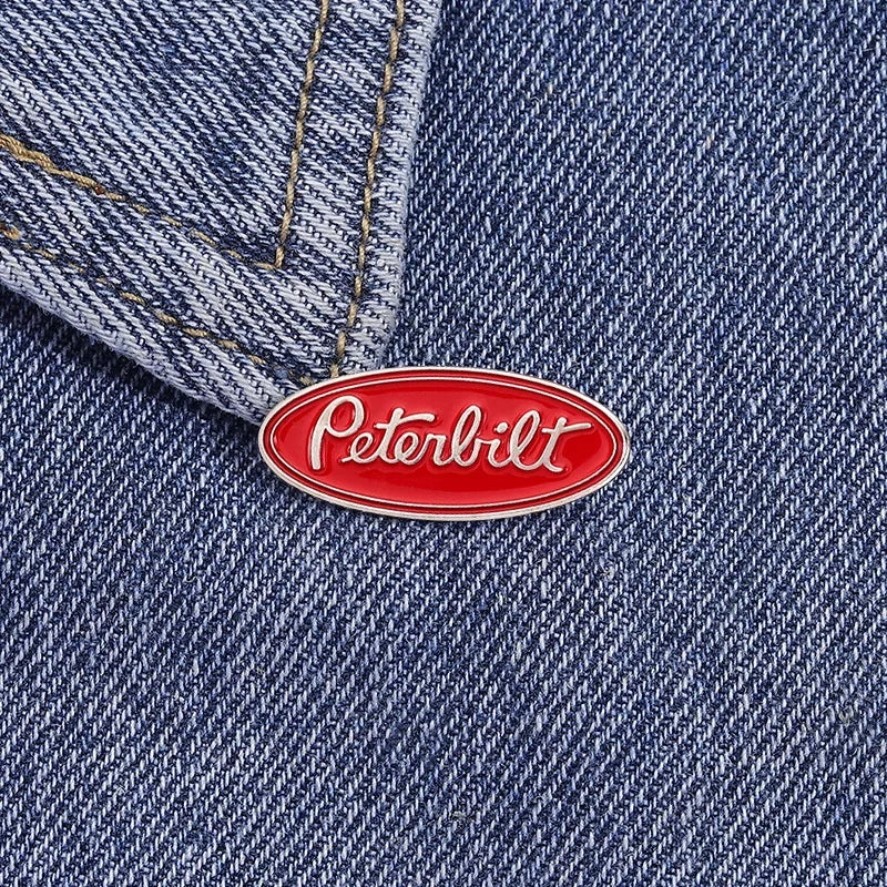 A red oval enamel lapel pin featuring the Peterbilt logo on a dark blue denim fabric.