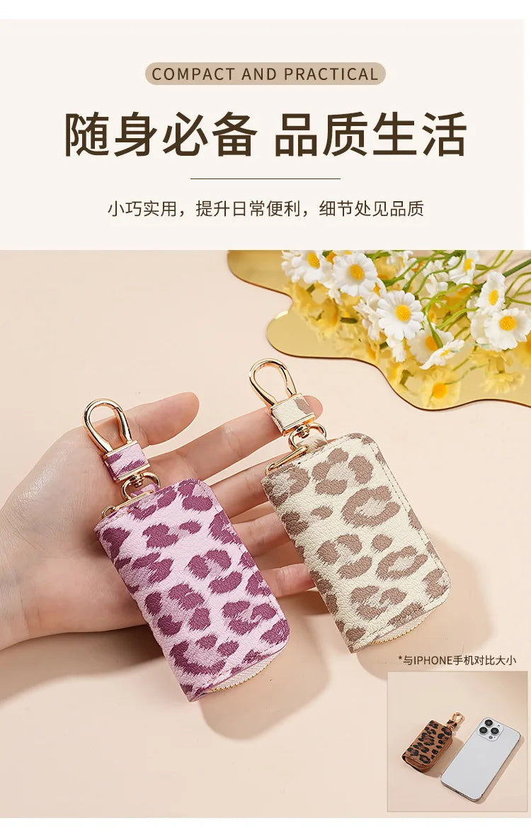 A hand holds a small leopard print fabric key holder attached to a gold-colored metal ring.