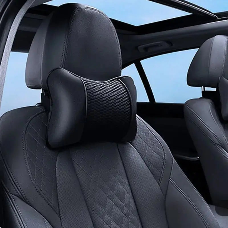 Close-up view of a black car seat headrest neck support cushion with quilted leather upholstery.