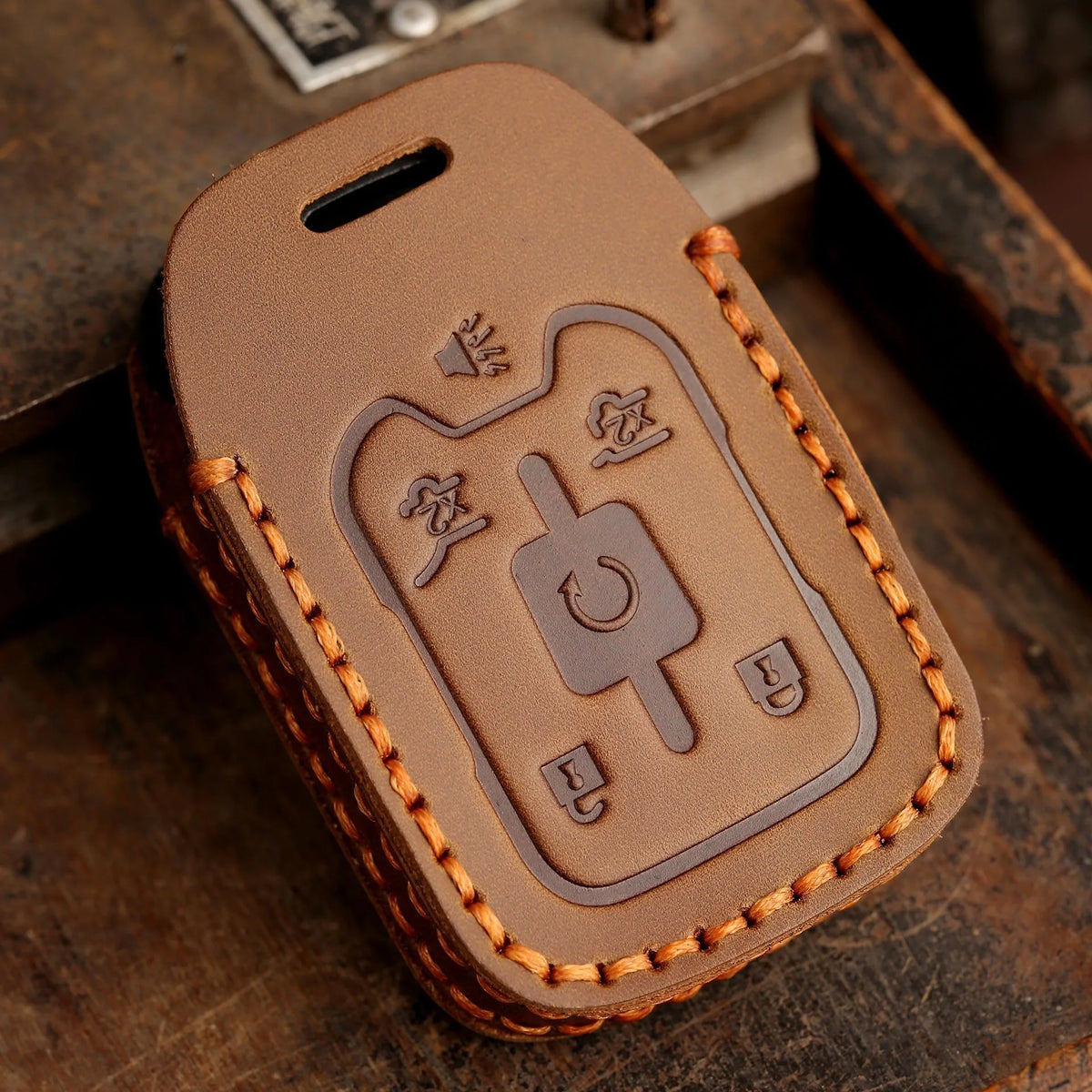 A brown leather key cover with embossed symbols for Chevrolet and GMC trucks resting on a wooden surface.