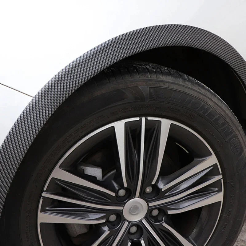 Close-up view of a black alloy wheel with a polished rim and carbon fiber fender trim.