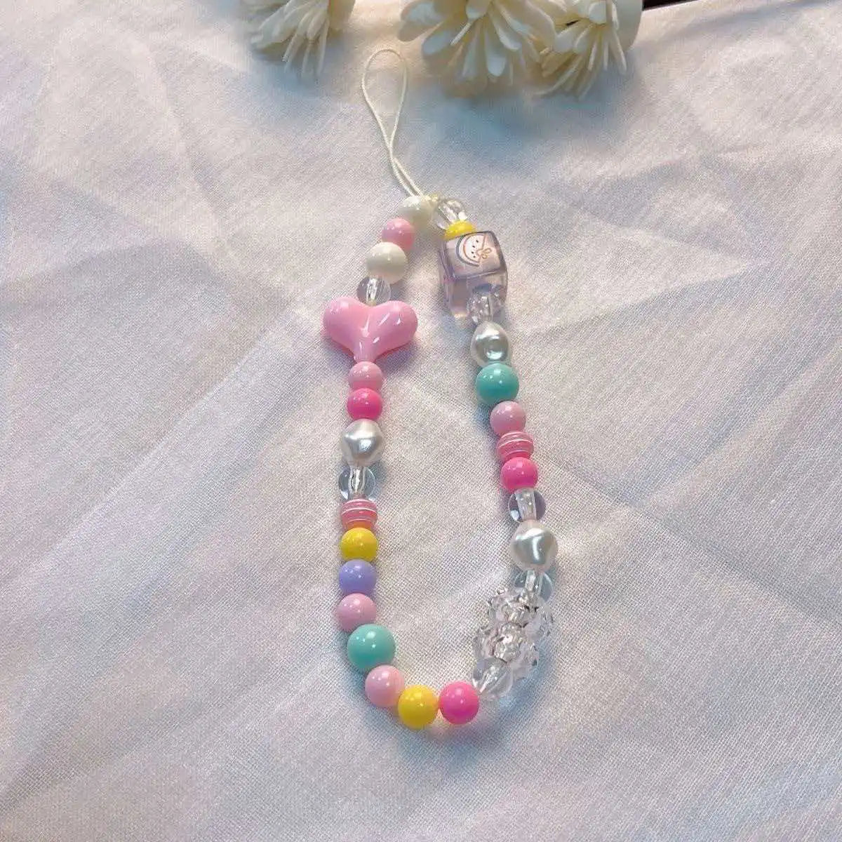 A lanyard featuring a round bead pendant with various colored beads and a charm on a white fabric background.