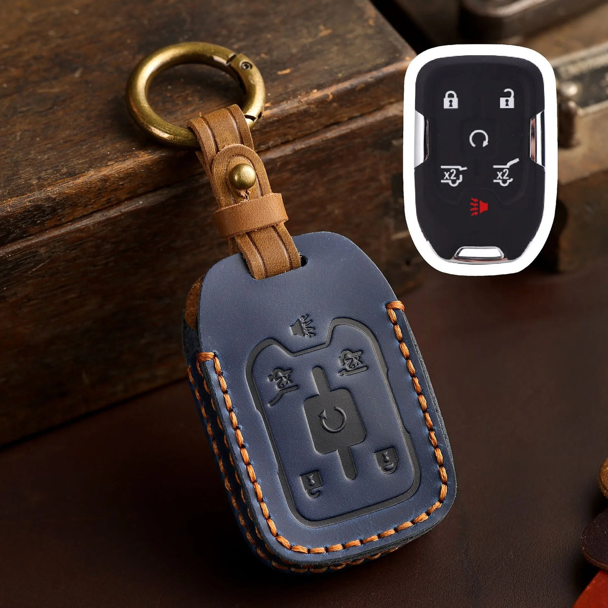 A dark blue leather key cover with a brass ring attached, resting on a wooden surface next to a white electronic key fob.