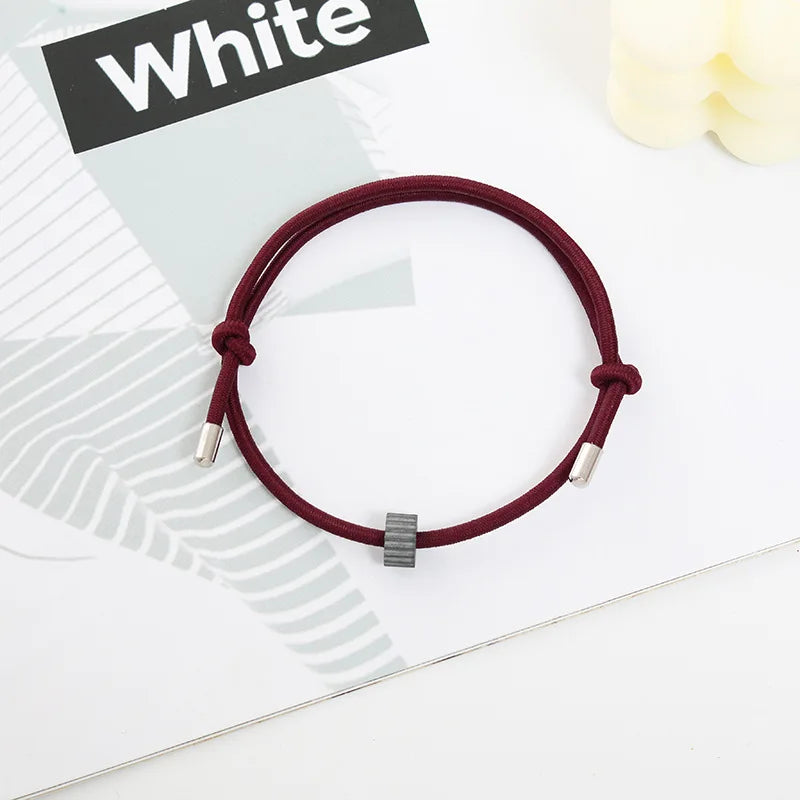 A maroon heart-shaped fitness tracker bracelet is displayed on a white background next to a piece of paper.