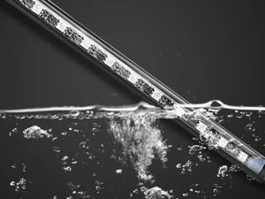Gros plan d'une bande lumineuse sans fil multicolore de voiture en cours de test, avec de l'eau qui éclabousse la bande.