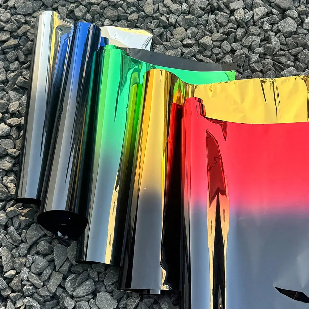 A collection of two-tone gradient car window tint film rolls displaying a spectrum of colors from black to yellow and red.