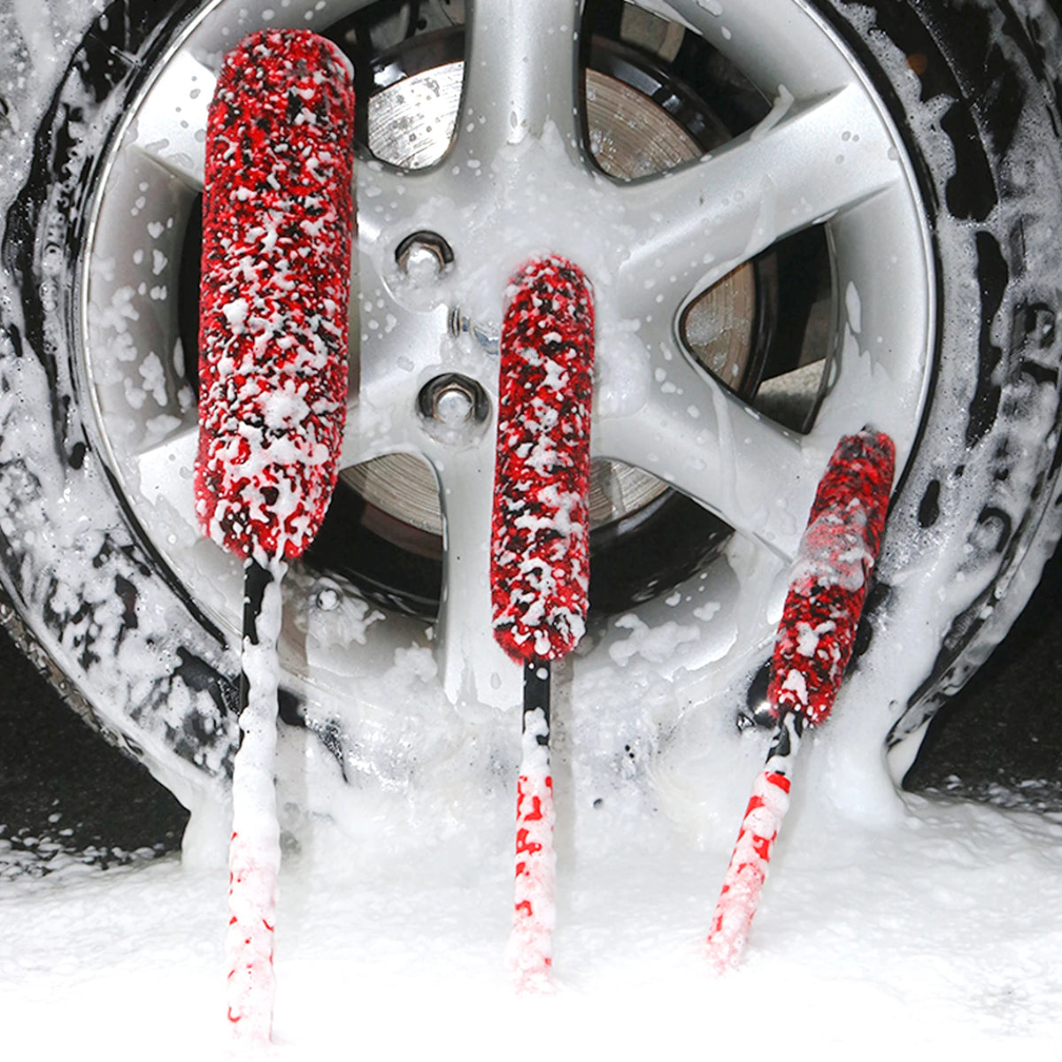 A close-up of three red wool cleaning brushes resting on a tire surrounded by white foam.