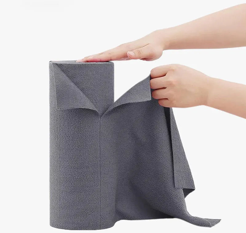 A hand is holding a gray reusable microfiber cleaning towel, showing its texture and folded shape.