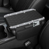 A black car console cover with a diamond grid pattern and a silver accent, resting in a dark interior.