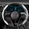 Nahaufnahme eines schwarzen Lenkrads mit einer weißen, gemusterten Abdeckung im Autointerieur.