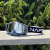 Une paire de lunettes de sport grises avec une sangle noire et le logo NAFF, posées sur une surface claire parmi le feuillage