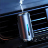 A silver portable car air freshener is shown emitting a plume of white smoke from a vent.