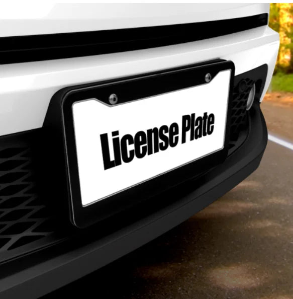 إطار لوحة أسود مع لوحة بيضاء تحمل عبارة 'License Plate' مثبت على مصد سيارة أبيض.