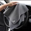 A gray multi-sided coral fleece drying towel is being held in the interior of a car.