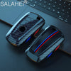 Un juego de fundas para llaves de coche de fibra de carbono negro y azul sobre una superficie oscura junto a un teclado de po