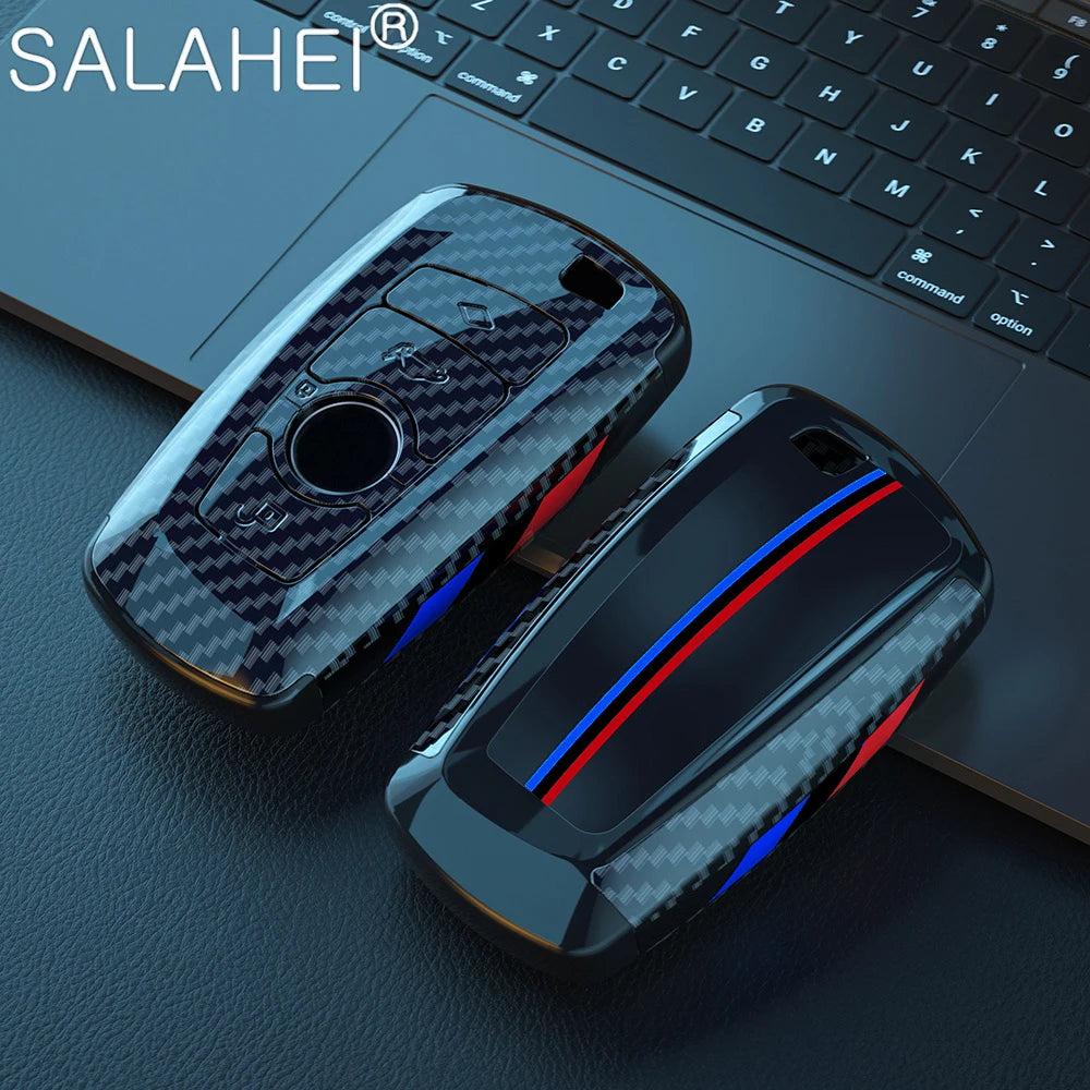 Un juego de fundas para llaves de coche de fibra de carbono negro y azul sobre una superficie oscura junto a un teclado de po