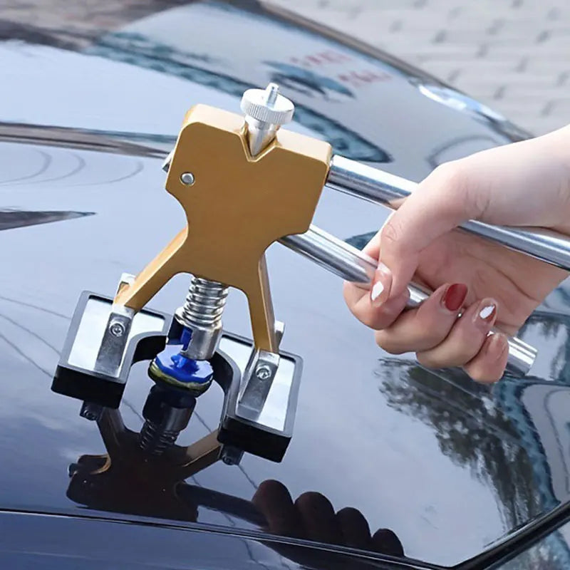 A hand is using a gold-colored professional car dent repair puller kit to remove a dent from a car's body.