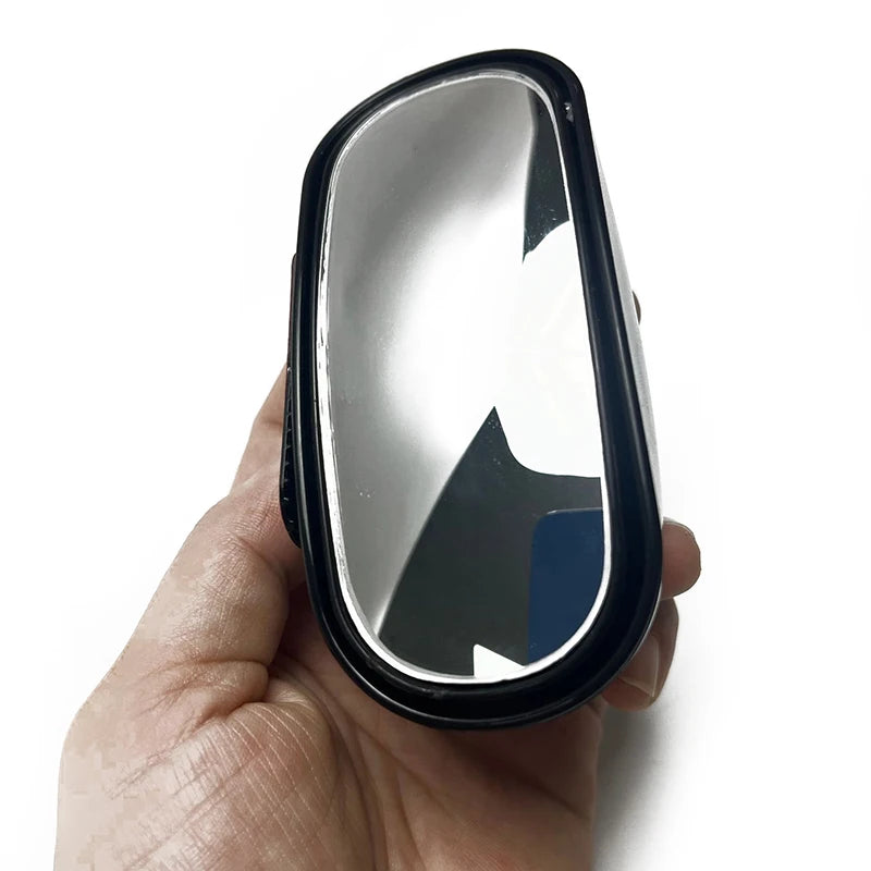 A hand holds a black car blind spot mirror with a silver reflective surface.